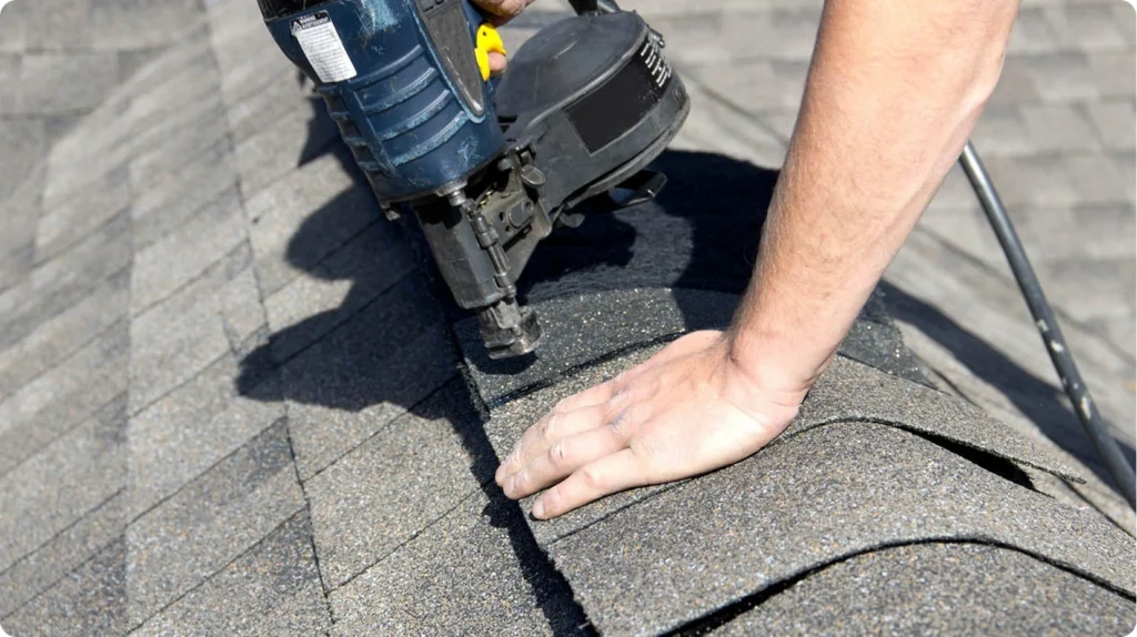 Roofer installing asphalt shingles with nail gun